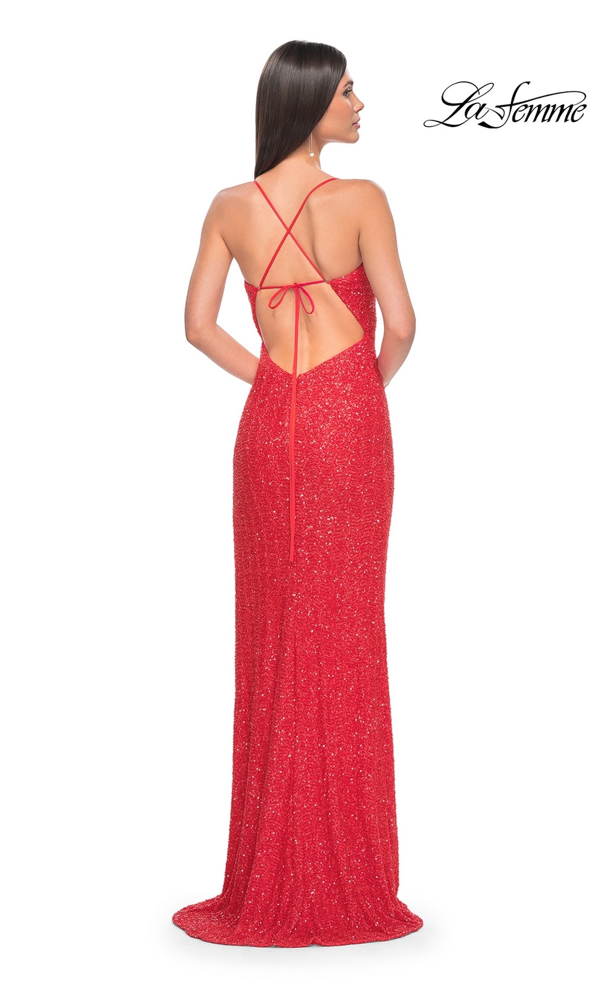 A woman wearing the La Femme Hot Coral Long Beaded Prom Dress 31432 with sparkly beading and thin crisscross straps stands facing away. The